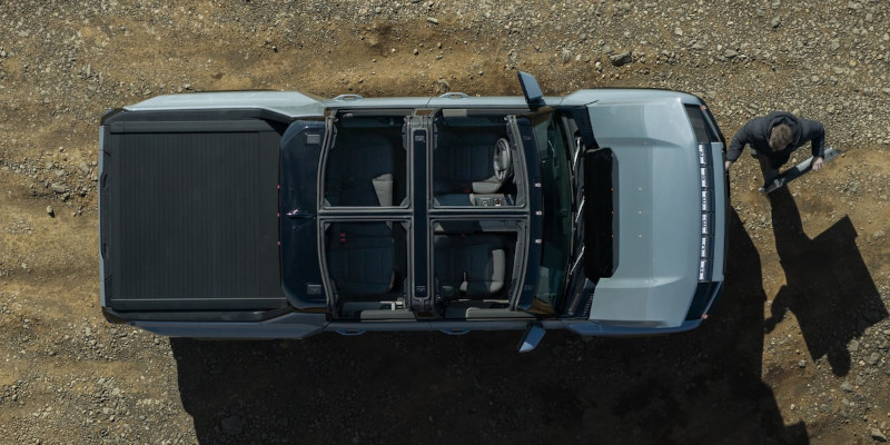 Aerial view of a light blue 2025 GMC HUMMER EV Pickup with a removable roof, parked on dirt.