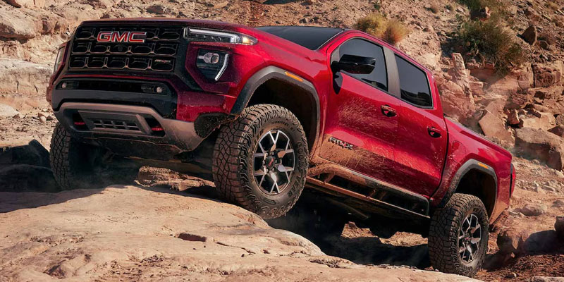 Red GMC Canyon truck climbing a rocky terrain in an outdoor setting.